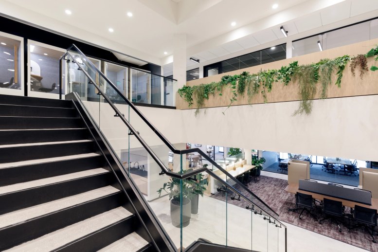 Spacious bi-level lobby at 3390 Mary Street with a black staircase, glass railings, and lush hanging greenery.