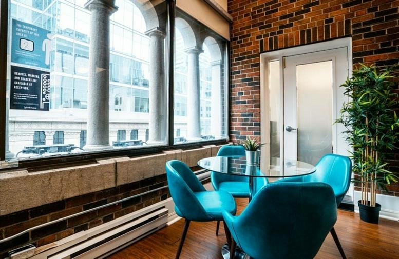 Sunny break area at 350 Bay St with teal chairs, brick walls, and arched windows.