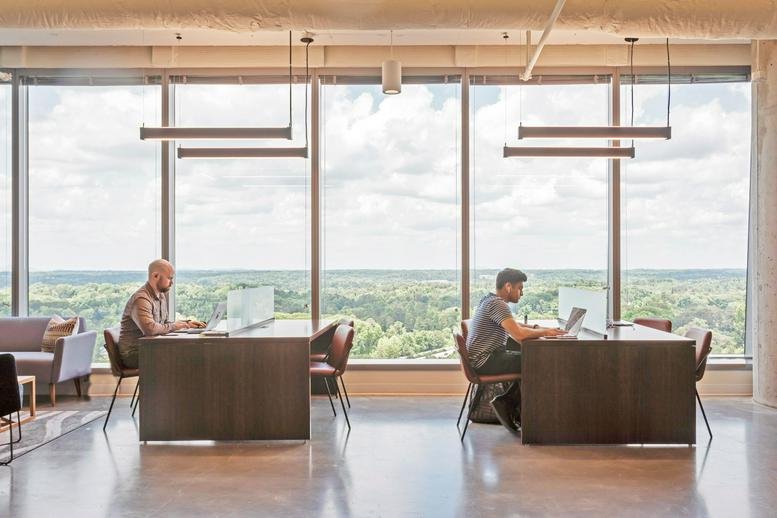Spacious communal coworking area at Three Aliance Center with long desks and floor-to-ceiling window views.