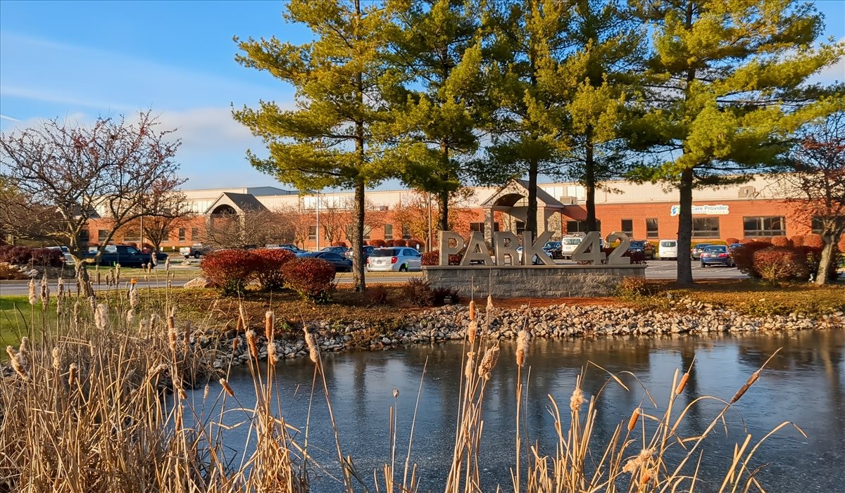 Exterior view of the brick facade building at 3600 Park 42 Drive with lush greenery and a pond.