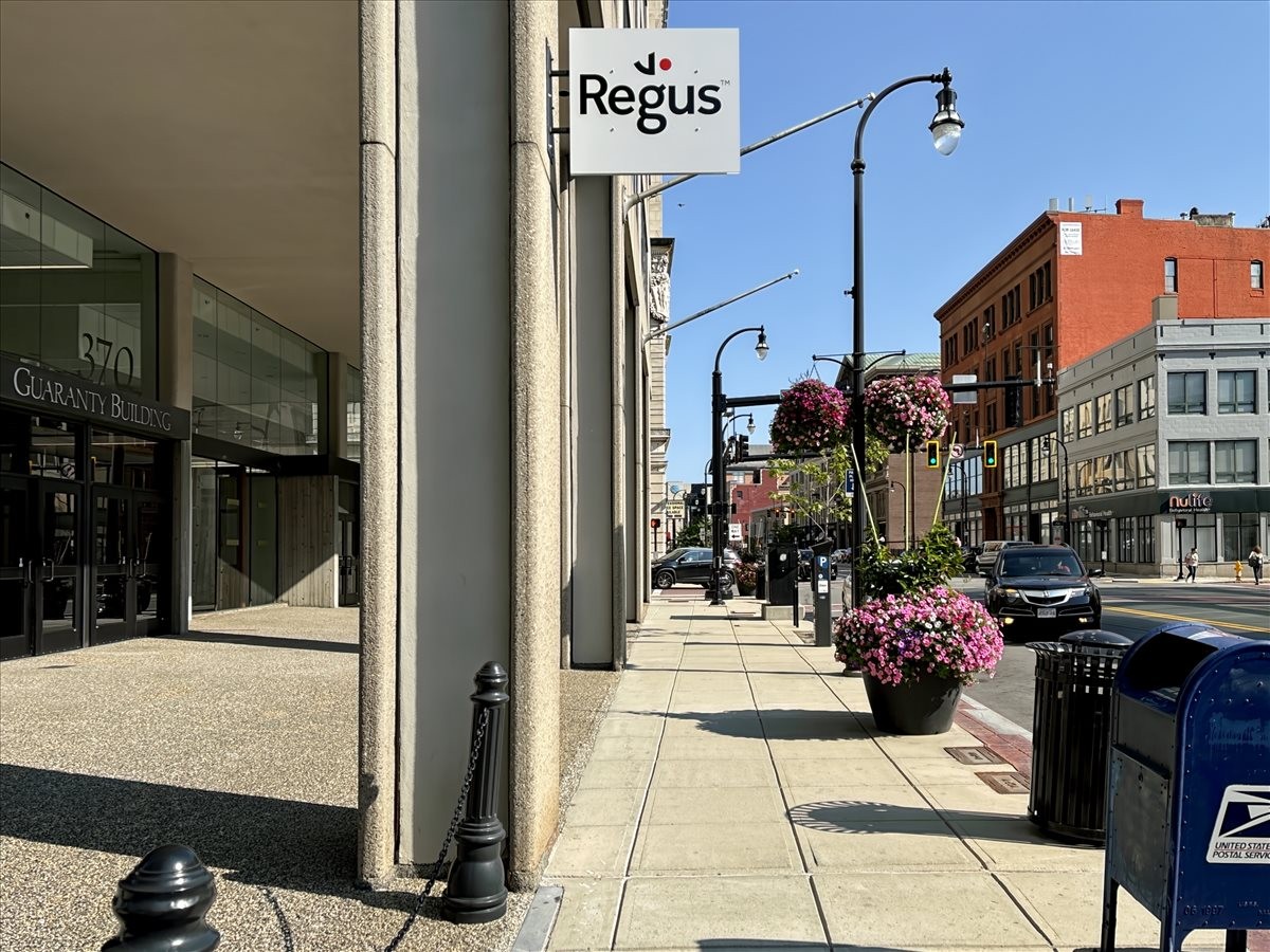 Modern building exterior with a Regus sign above a busy sidewalk with colorful flower planters.