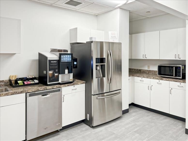 Modern office kitchen with stainless steel refrigerator, coffee station, and white cabinetry.
