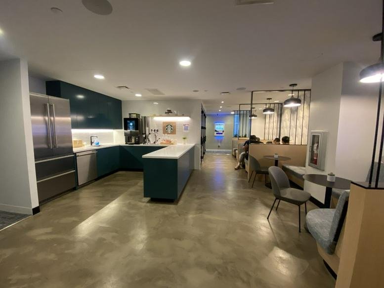 Sleek communal kitchen and breakout area with teal cabinetry and polished concrete floors.