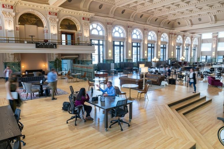 Grand, open-plan coworking hall with high vaulted ceilings and arched windows.