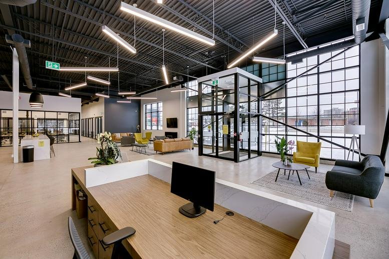 Spacious reception area with a modern desk, lounge seating, and an industrial glass elevator.
