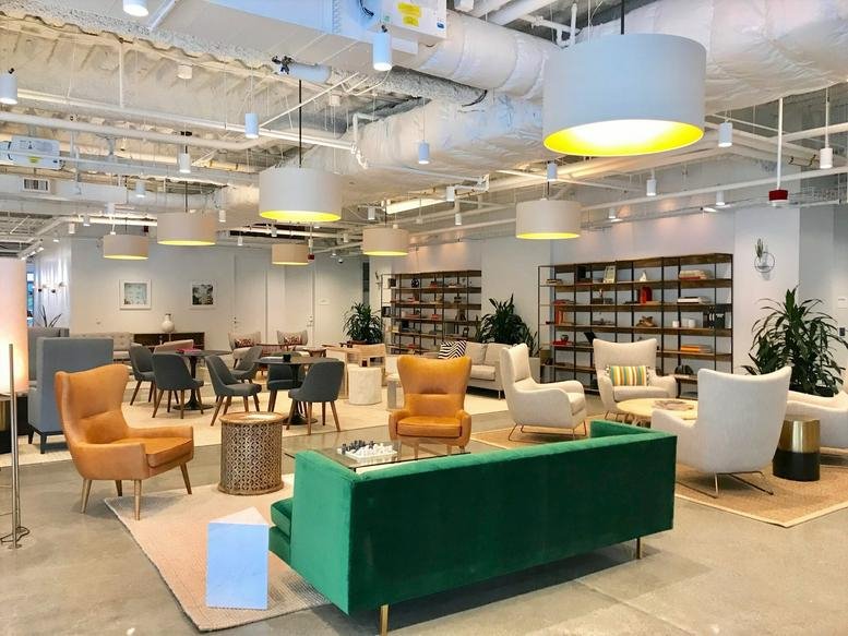 Spacious lounge with a green velvet sofa, tan leather armchairs, and bookshelves.