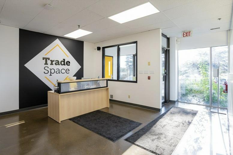 Bright reception area at 4121 23B Street NE with a branded Trade Space feature wall and wooden desk.