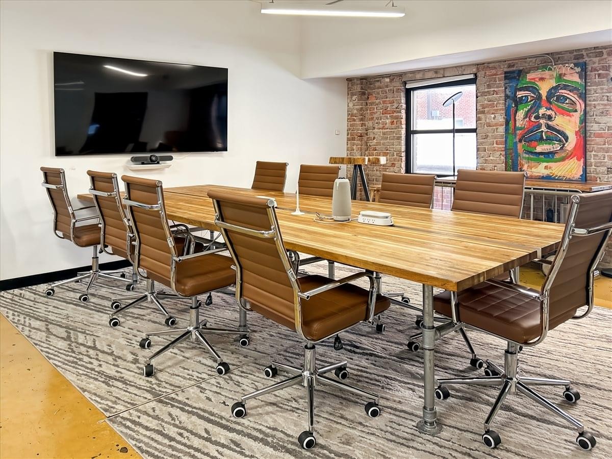 Meeting room at 414 Fayetteville St featuring a large wooden table, leather chairs, and brick feature wall.