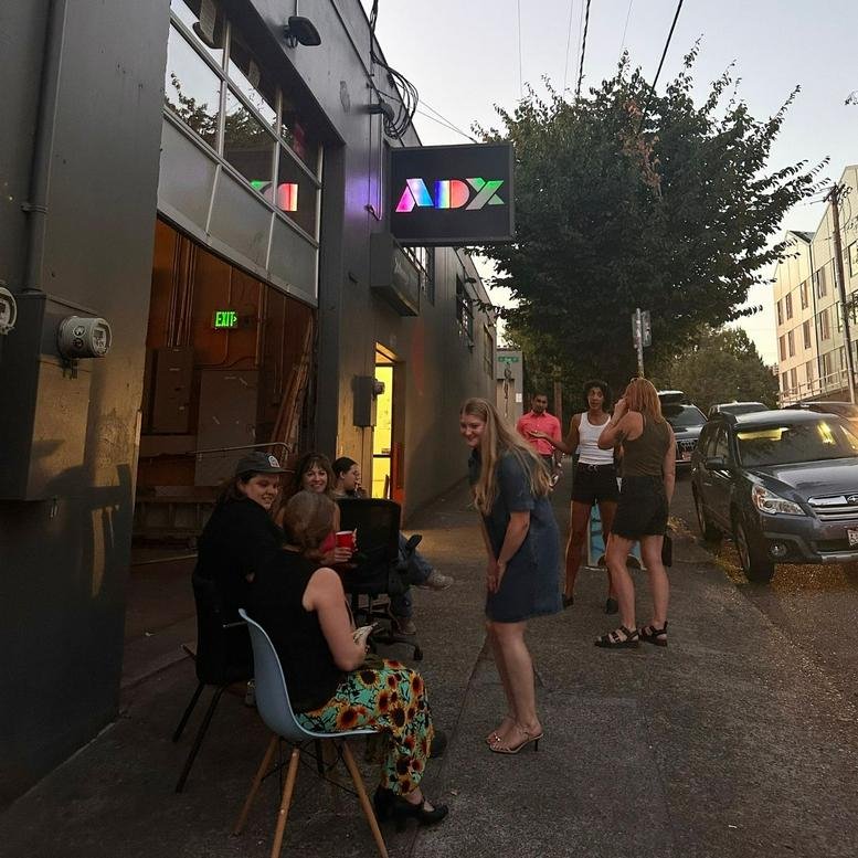 Exterior entrance of 417 SE 11th Avenue, Portland (Oregon) with glowing ADX sign and people gathering.