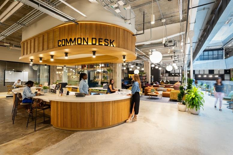 Modern reception area at Common Desk featuring a curved wood-slat desk and hanging globe lights.