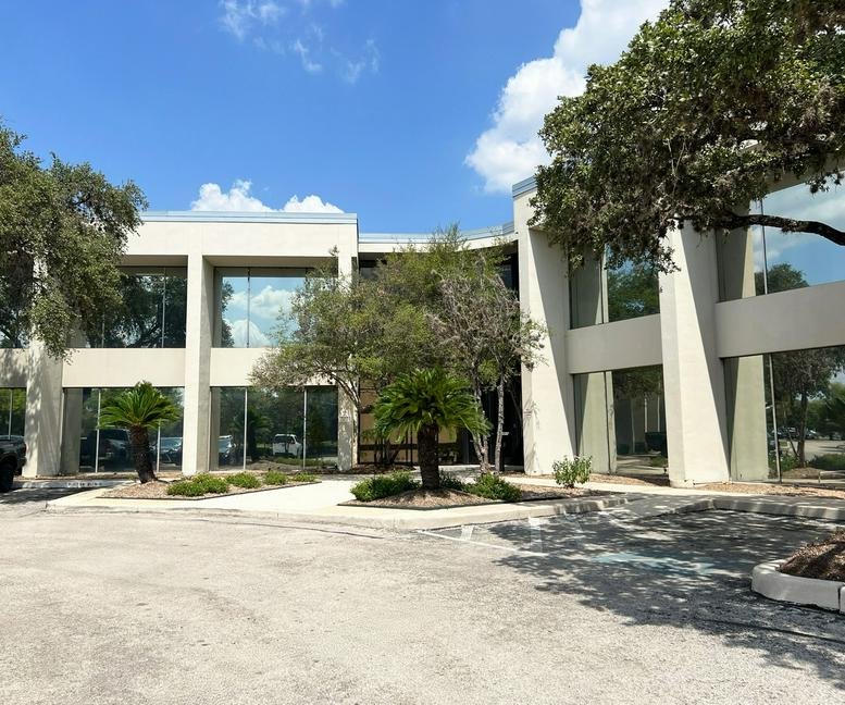 Exterior view of the office building at 4241 Woodcock Dr featuring white columns and green landscaping.