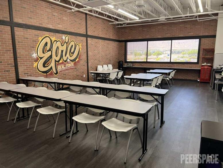 Spacious training room with multiple rows of tables, white chairs, and an Epic mural on a brick wall.