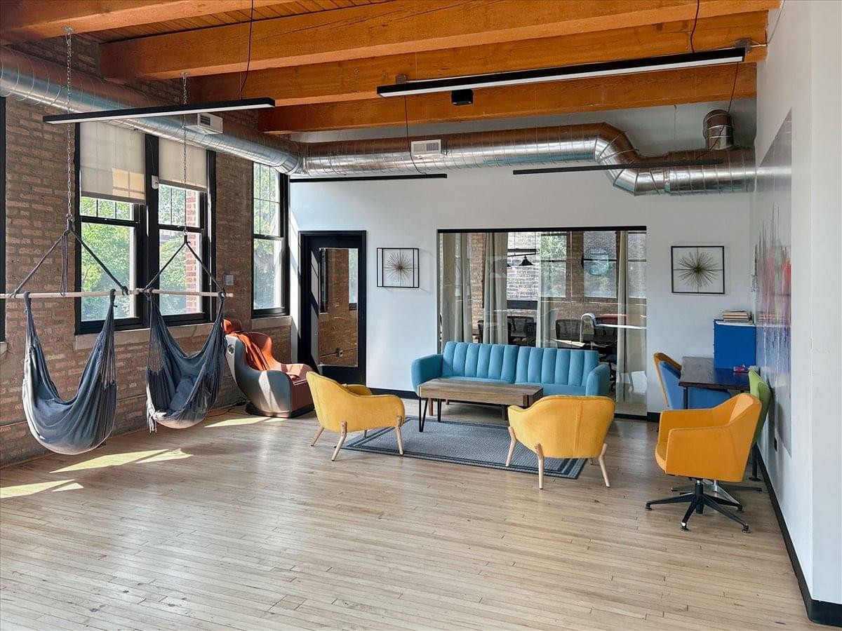Creative breakout area with blue sofa, yellow armchairs, and hanging hammock swings under a timber ceiling.
