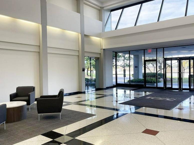 Spacious modern building lobby with polished tile floors and large floor-to-ceiling glass windows.