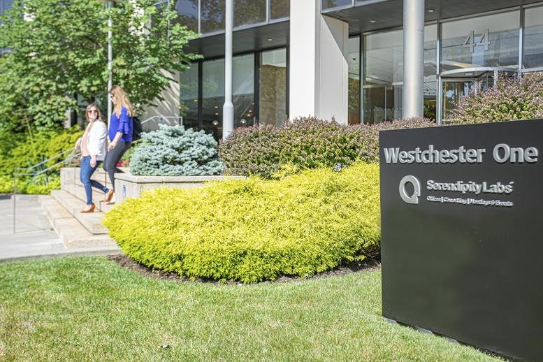 Exterior view of the landscaped entrance at Westchester One with a black monument sign.