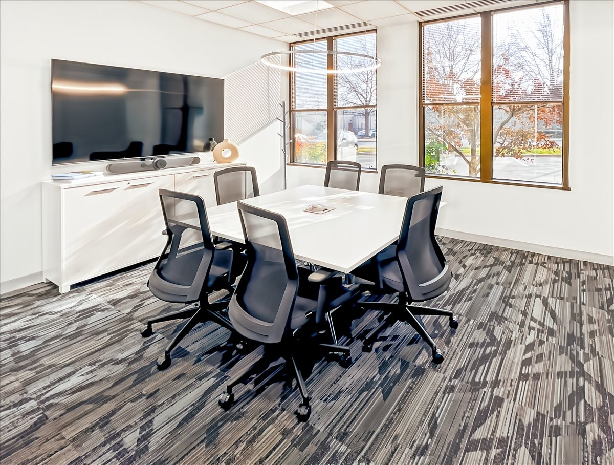 Meeting room at 50 Catoctin Circle NE, Suite 101 with a white table, mesh chairs, and wall-mounted TV.