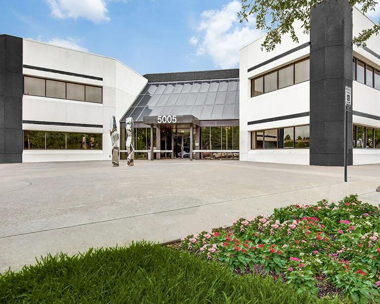 Modern exterior entrance of 5005 West Royal Lane with a glass atrium and landscaped flower beds.