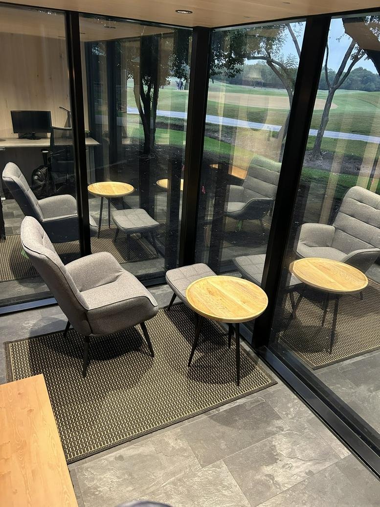 A light-filled lounge area at 501 Twin Creeks Drive featuring grey armchairs and wooden side tables.