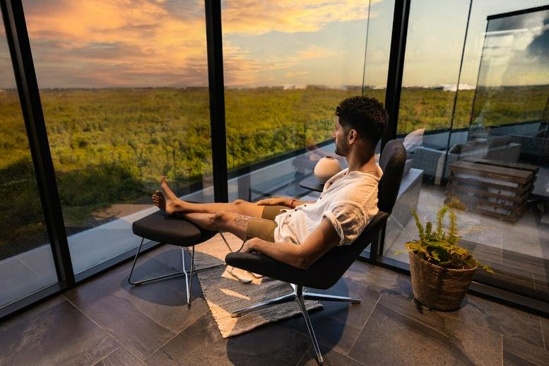 Man relaxing in a modern black lounge chair overlooking a sunset landscape.