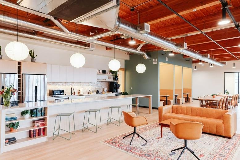 Modern kitchen and breakroom area with white cabinetry, a large island, and orange accent chairs.