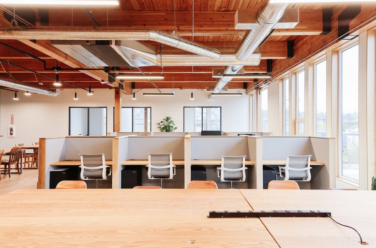 Open-plan workspace with semi-private cubicles and exposed ductwork on a timber ceiling.