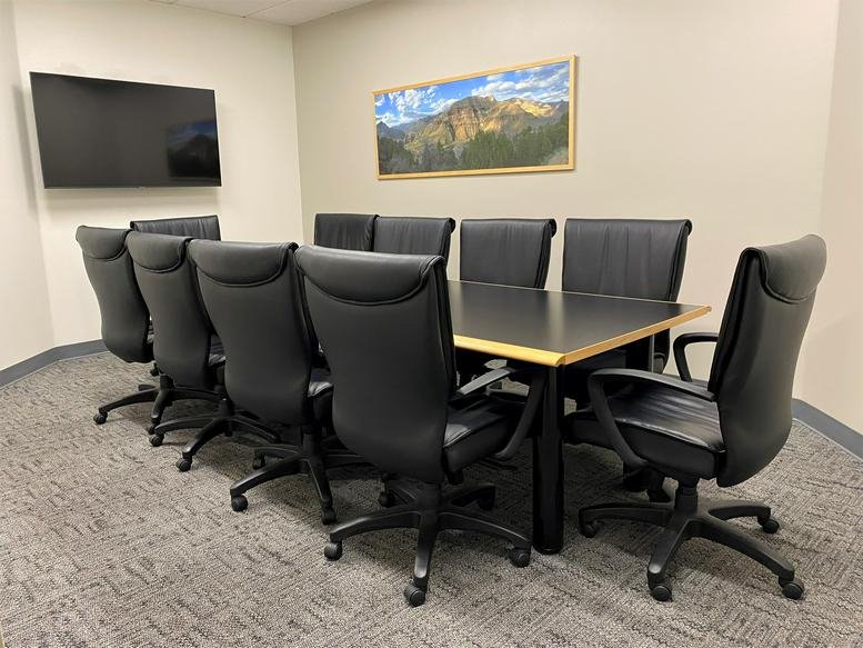 Spacious boardroom with a long table and eight black leather chairs.