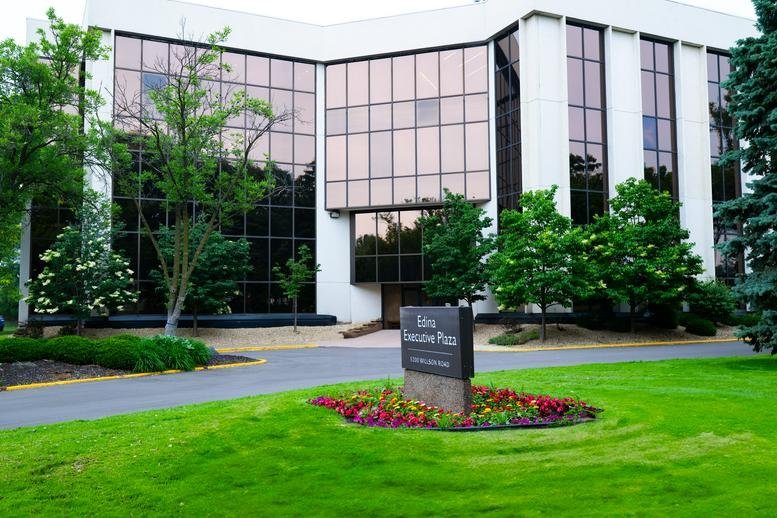 Exterior view of the multi-story glass-fronted 5200 Willson Road building in a lush green landscape.