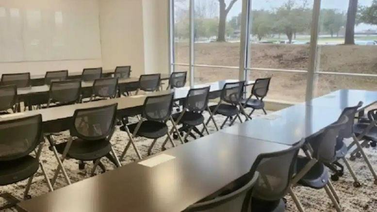 Training room setup with rows of black chairs and long tables facing a window.
