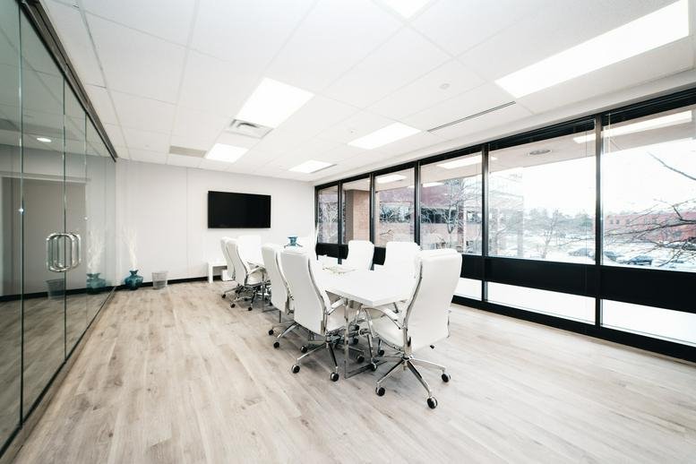 Spacious conference room featuring white chairs and a glass wall overlooking the outdoors.