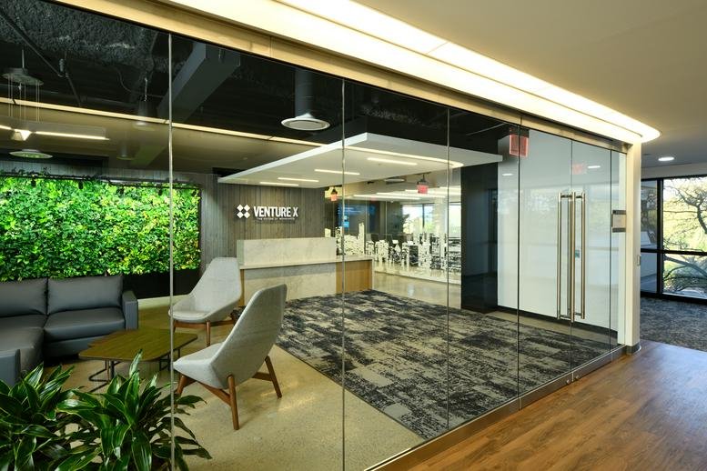 Modern lobby with glass partitions, a green moss wall, and stylish lounge chairs.