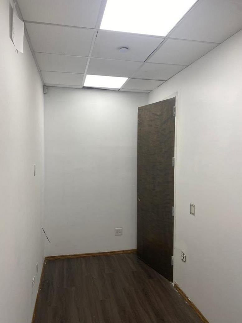 Compact private office at 580 5th Avenue, Suite 210 with wood-look flooring and bright LED ceiling panels.