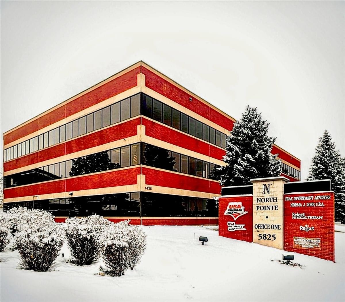 The red and tan multi-story exterior of 5825 Delmonico Drive, Colorado Springs in a snowy setting.