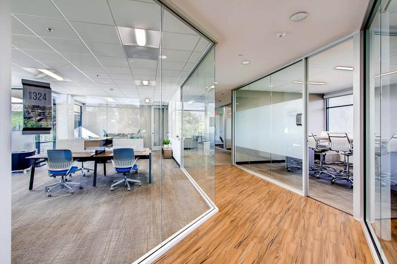 Bright office hallway with glass partitions and polished wood-style flooring.