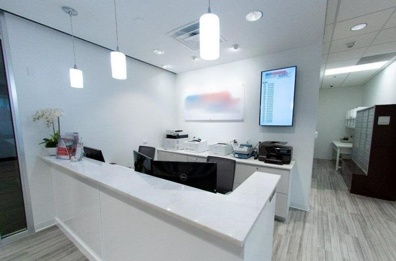 A modern white reception desk at 6000 Metrowest Boulevard Suite 200 with hanging pendant lights and a digital display.
