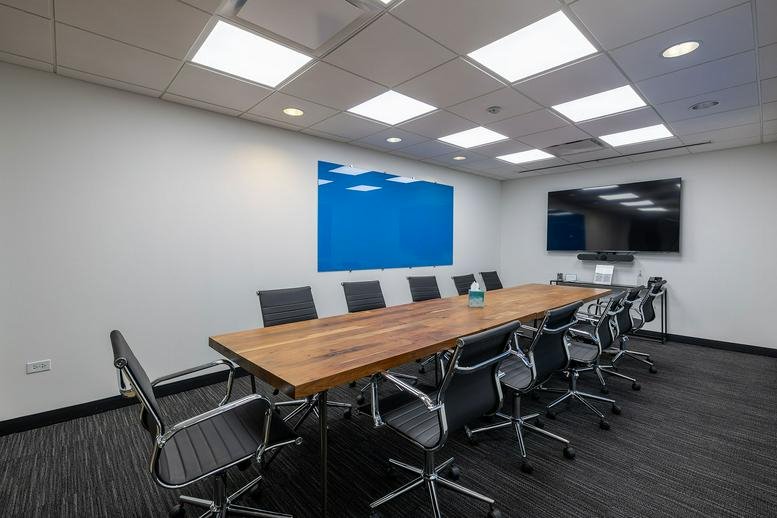 Boardroom with a long wooden table, blue feature wall, and wall-mounted screen.
