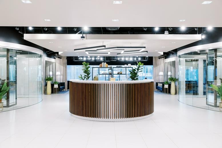 Circular wooden reception desk centered in a bright, modern open lobby.