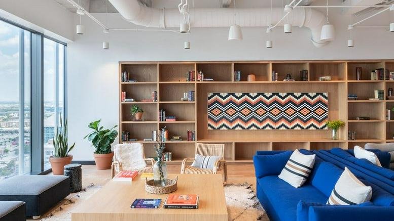 Bright common area at 609 Main Street, Houston, Texas with a blue sofa, bookshelves, and geometric art.
