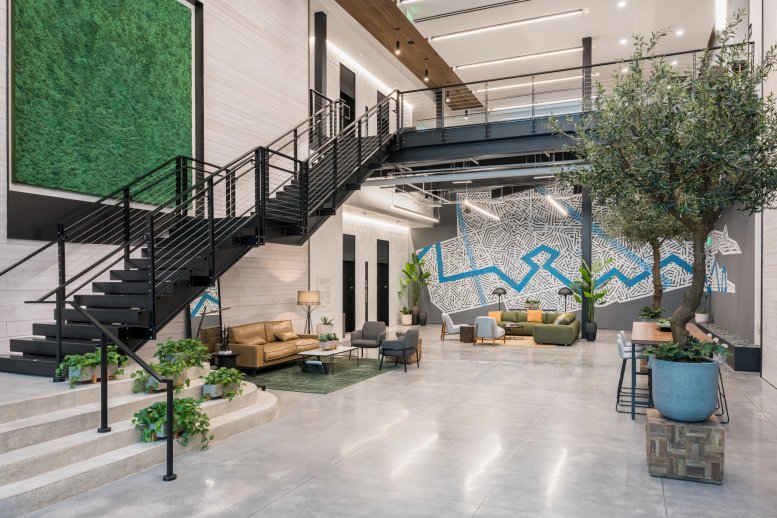 Double-height lobby with a grand staircase, moss wall, and various seating clusters.