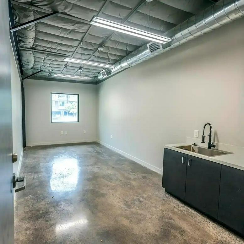 Spacious private office with concrete floors, exposed ceiling, and a sink with cabinets.