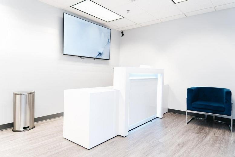 White minimalist reception area at 6340 Security Boulevard, Suite 100 featuring a wall-mounted TV and blue velvet chair.
