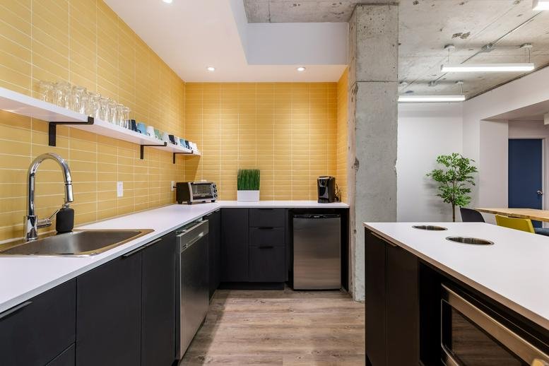 Modern communal kitchen at 65 Rue Principale with yellow tiled walls and dark cabinetry.