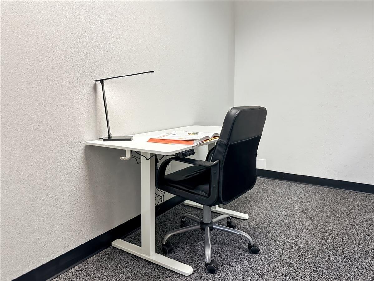 Single workstation with a white desk, black office chair, and modern desk lamp.