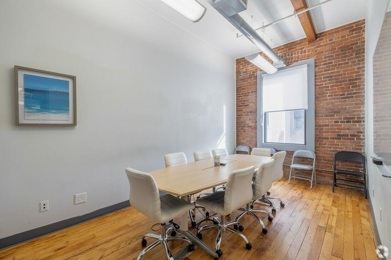 Modern conference room with a light wood table, white chairs, and an exposed brick wall.