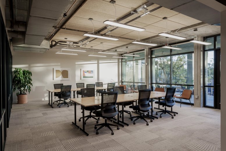 Modern open-plan office at 7001 Burnet Road featuring long wooden desks and large windows.