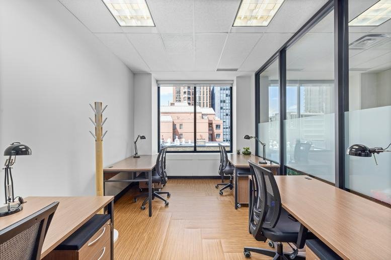 Bright office suite at 77 Bloor Street West with multiple wood-topped desks and ergonomic chairs.