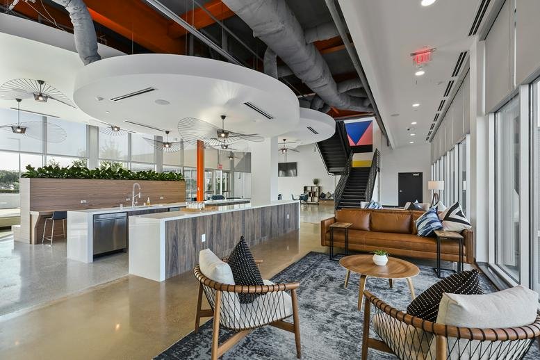 Spacious communal lounge at 7701 Lemmon Avenue with leather sofas, modern chairs, and a kitchen island.
