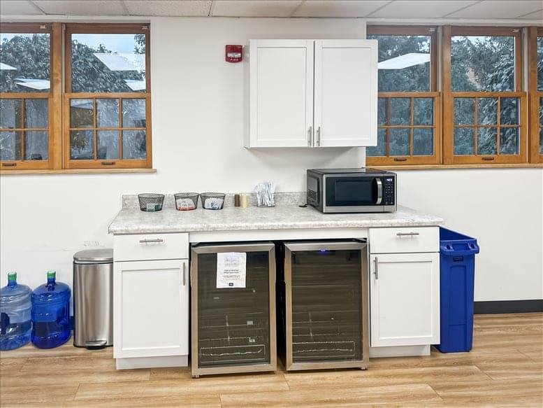 Office kitchenette with white cabinetry, microwave, and beverage coolers under a stone-effect countertop.