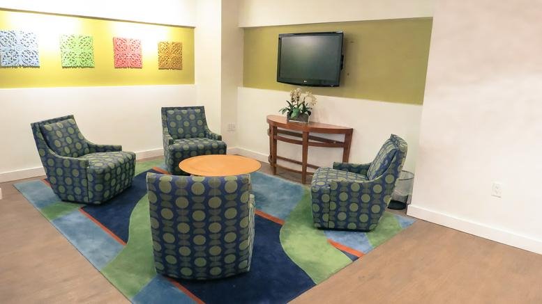 Colorful lounge area with blue patterned armchairs and a wall-mounted TV at 8200 Greensboro Drive, Suite 900.
