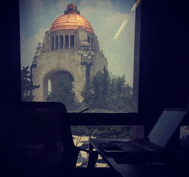 Office workspace with a desk and laptop featuring a framed view of the Monumento a la Revolución at 9, Avenida de la República.