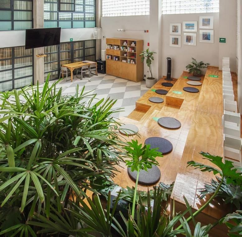 Expansive communal space featuring tiered wooden seating with cushions and lush indoor greenery.